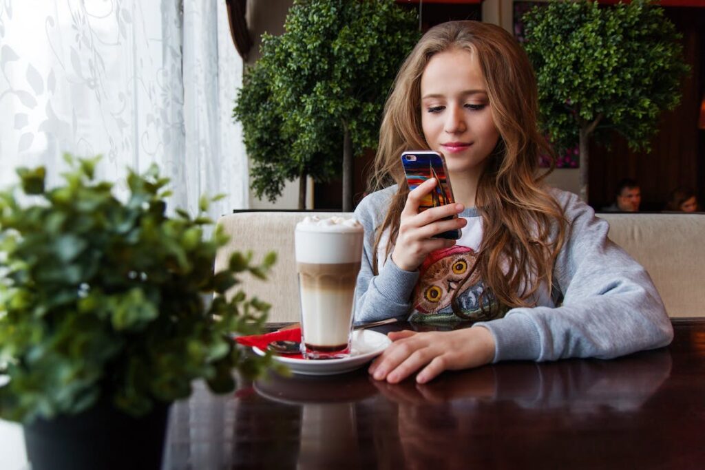 Young woman sitting looking at her phone with cold latte on the table