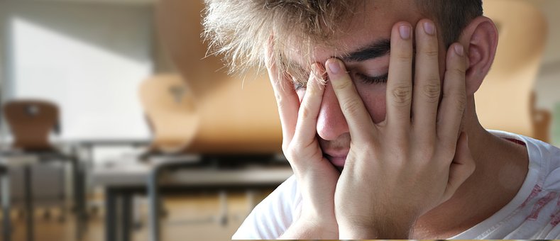 Teen male with head in his hands, eyes closed and looking despondent